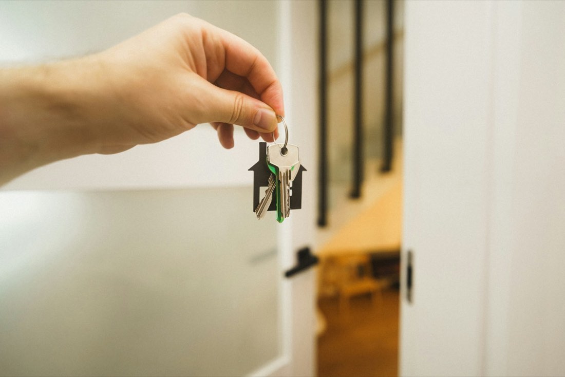 A hand holding a set of house keys at a front door